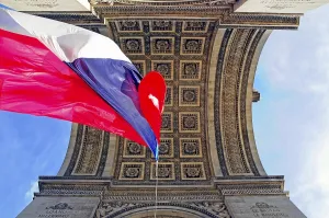 View from below into the Arc de Triomphe with a waving French flag