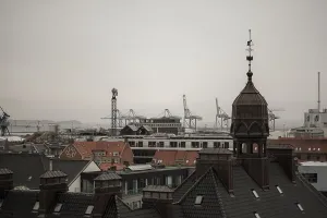 View of a cityscape with rooftops and cranes in the distance under an overcast sky in Aarhus