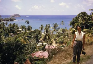 View over corrugated iron roofs of houses to tropical sea, British woman tourist posing, Trinidad and Tobago 1961-1963