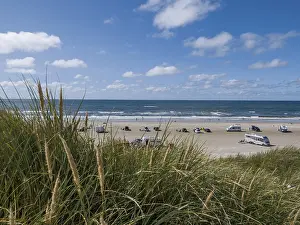 View over dunes to a car beach on the North Sea with campervans by the sea under a blue sky