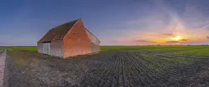 View of a field on which a rural building made of baked stone stands at sunset