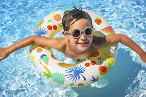 July 2024 Prints: Top view of a happy young boy inside a blue swimming pool with swim goggles and a float