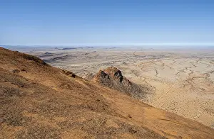 View from a hill over the endless dry desert landscape under blue sky