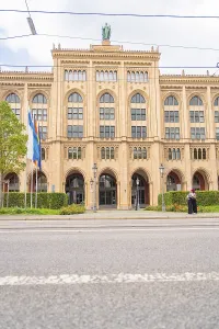 Front view of an imposing historic building with flags and green plants