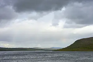 View of a lake with distant hills and rainbows on cloudy sky