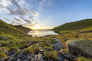 View of a lake at sunrise, surrounded by grassy hills and rocks