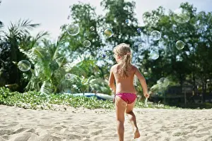 Back view of little happy girl playing soap bubbles on the topical beach