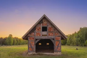 View of an open half-timbered barn standing on a pasture in the sunset