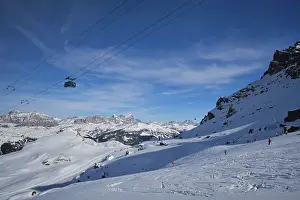 View of a ski resort piste with people skiing in Dolomites in Italy with cable car ski lift