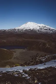View of a snow-capped mountain and a lake in a rocky landscape under a blue sky
