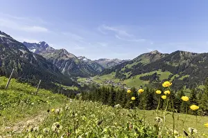 View down the valley to the village of Mittelberg with yellow flowers and mountain peaks in Kleinwalsertal