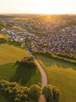 View of a village and a road surrounded by fields and trees at sunset