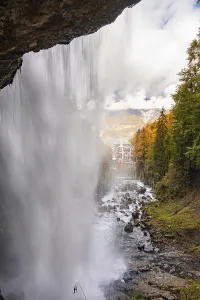 View through a waterfall onto an autumn landscape with mountains and a building