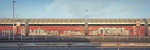 Category Historic EN Prints: View over a weathered crash barrier to a part of a goods wagon that has been painted with graffiti