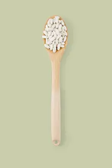 Top view of wooden spoon full of white beans on a green background