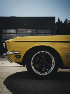 Side view of a yellow classic car in front of a modern garage in sunlight
