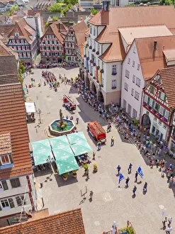 Viewed from above, a parade passes half-timbered houses around a central fountain