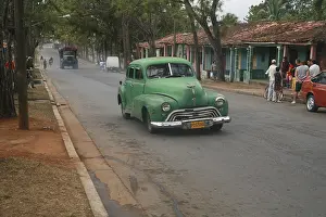Vintage car driving through a street scene in Vinales
