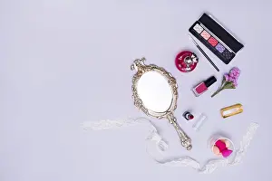 Vintage hand mirror lipstick nail varnish sponge perfume bottle eyeshadow palette purple background