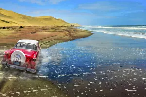 Category Oldtimer Prints: A vintage pink car on a sandy road with dunes and ocean background