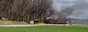 A vintage steam train releases smoke as it moves along the tracks