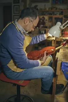 Violin maker inspecting the instrument under the light in his workshop crafting a stringed instrument using traditional