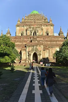 Visitors walk along a paved path that leads to a large temple