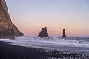 Volcanic formations on the black sand beach of Reynisfjara at sunset in Iceland