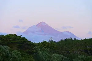 Volcano Mount Taranaki at dusk with clouds and surrounding vegetation