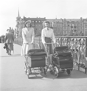 For a walk in the 1950s. Two women are out walking pushing prams in front of them