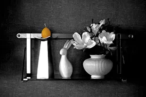 A wall shelf made of metal and glass serves as a base for various still lifes