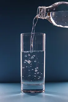 Water pours from a bottle into a glass on a blue background