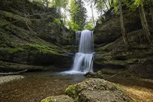 A waterfall in a forest with sunlight shining through the trees and moss-covered rocks