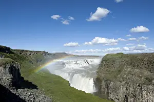Waterfall with rainbow falls into deep ravine