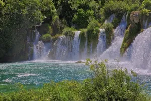 Waterfalls surrounded by dense vegetation and a clear river