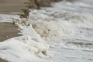 Wave breaks on beach and creates white foam on sandy shore