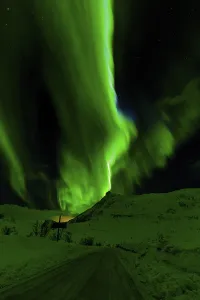 Waves of green aurora borealis light up the night sky above snow-covered hills