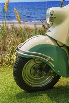 Front wheel of a cream-coloured scooter with turquoise accents on the beach
