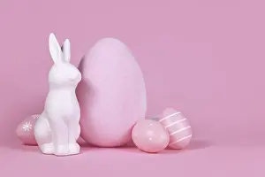 White bunny sculpture with easter eggs on pink background with copy space
