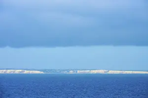White cliffs on the horizon under a cloudy blue sky over the sea