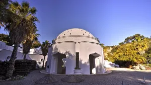 A white domed building in a peaceful setting with palm trees and clear skies