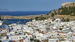 White houses of a harbour town with boats in the sea and a fortress in the background