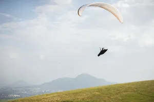 A white-orange paraglider flies over the mountainous terrain