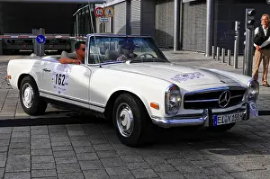 A white vintage Mercedes convertible on a street with two men in the vehicle