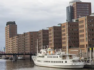 White yacht at a harbour with surrounding modern buildings and cloudy sky