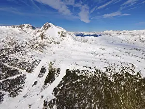 Wide-angle aerial view of snow-covered mountains and forest areas under a blue sky