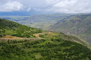 Wide green landscape with hills and a winding road under cloudy sky