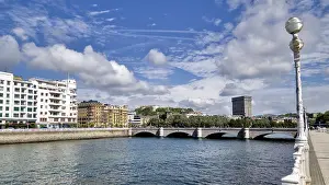 Framed Print : Wide view of a city bridge with river and surrounding buildings under a blue sky Framed Print : Wide view of a city bridge with river and surrounding buildings under a blue sky