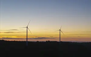 Two wind turbines in front of a calm sunset over a vast landscape