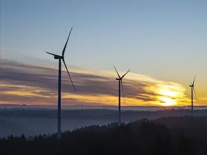Three wind turbines at sunrise over fog-covered forests